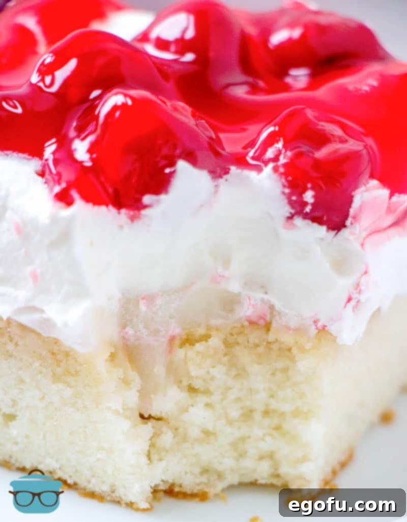 Ruby Snowdrift Cake 12 A close-up photograph of a slice of Cherries in the Snow Poke Cake on a white plate, with a bite taken out, revealing the creamy layers and moist cake texture.