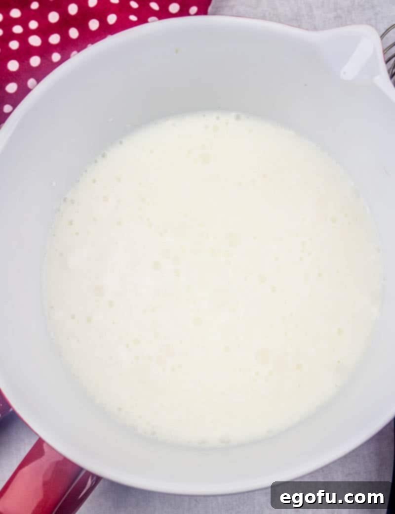 Ruby Snowdrift Cake 6 Instant white chocolate pudding mix being whisked with cold milk in a white bowl, showing the creamy texture forming.