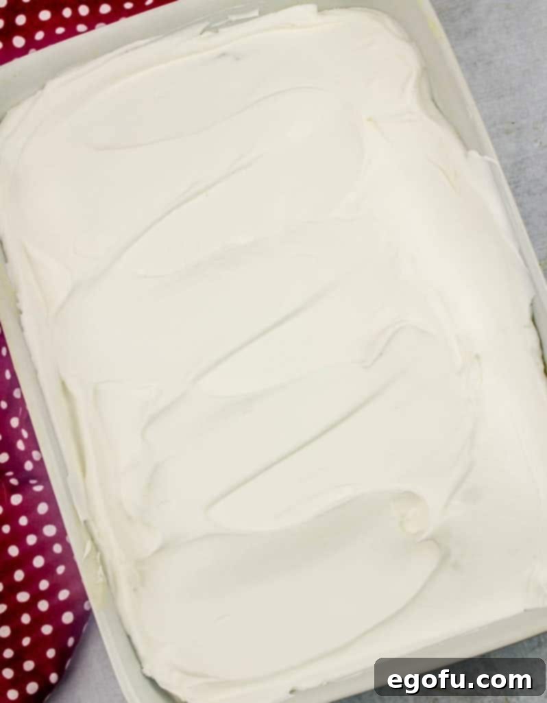 Ruby Snowdrift Cake 10 Thawed Cool Whip (whipped topping) being spread smoothly over the cooled pudding poke cake, creating a pristine white layer.