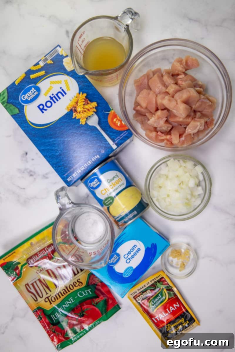 ingredients for creamy Italian chicken: boneless, skinless chicken breasts, chicken broth, Italian salad dressing mix, chopped onion, minced garlic, cream of chicken soup, cream cheese, rotini pasta, sun-dried tomatoes.