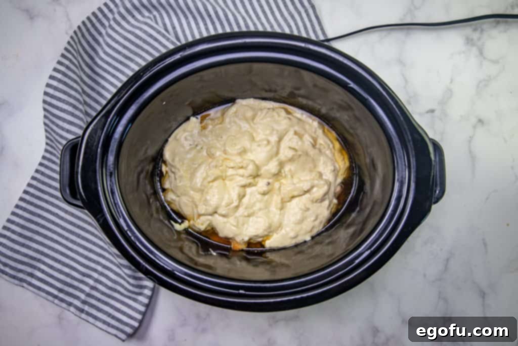 cream mixture added to cooked chicken mixture in black oval slow cooker.