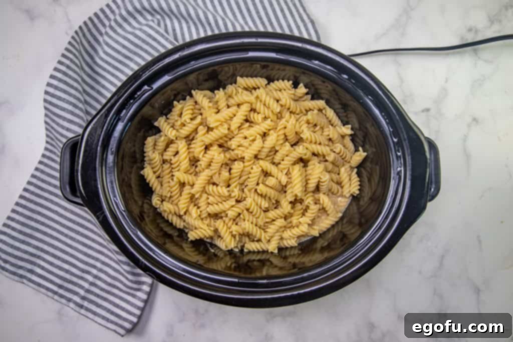 cooked rotini pasta added to creamy chicken mixture in slow cooker.