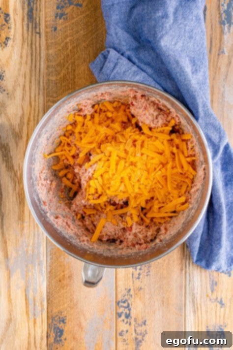 Cream Cheese Sausage Poppers 12 shredded cheddar cheese added to sausage and cream cheese mixture in a bowl.