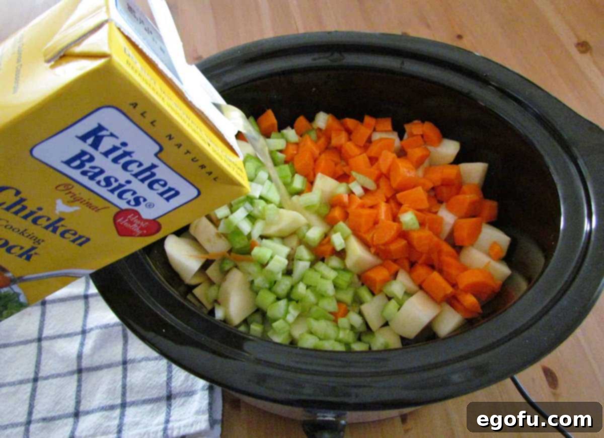 pouring Kitchen Basics chicken stock into slow cooker with diced vegetables.