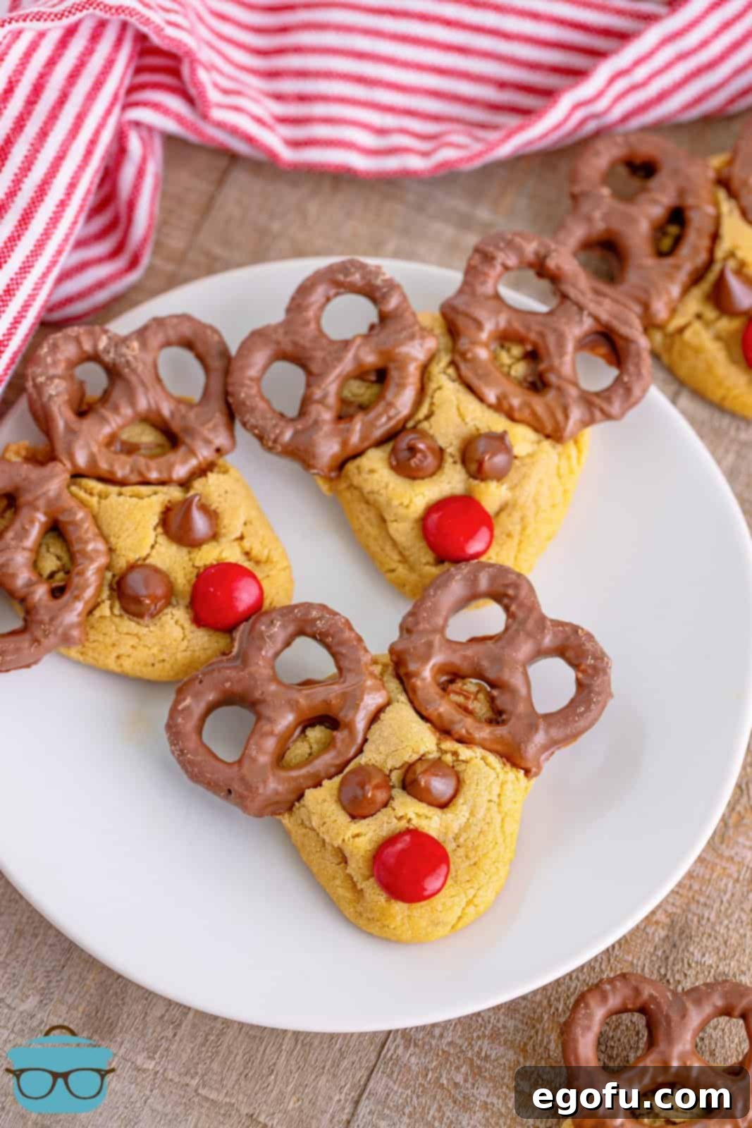 Red Nosed Reindeer Treats 14 three Reindeer cookies shown on a round white plate with a red and white striped dish towel in the background.