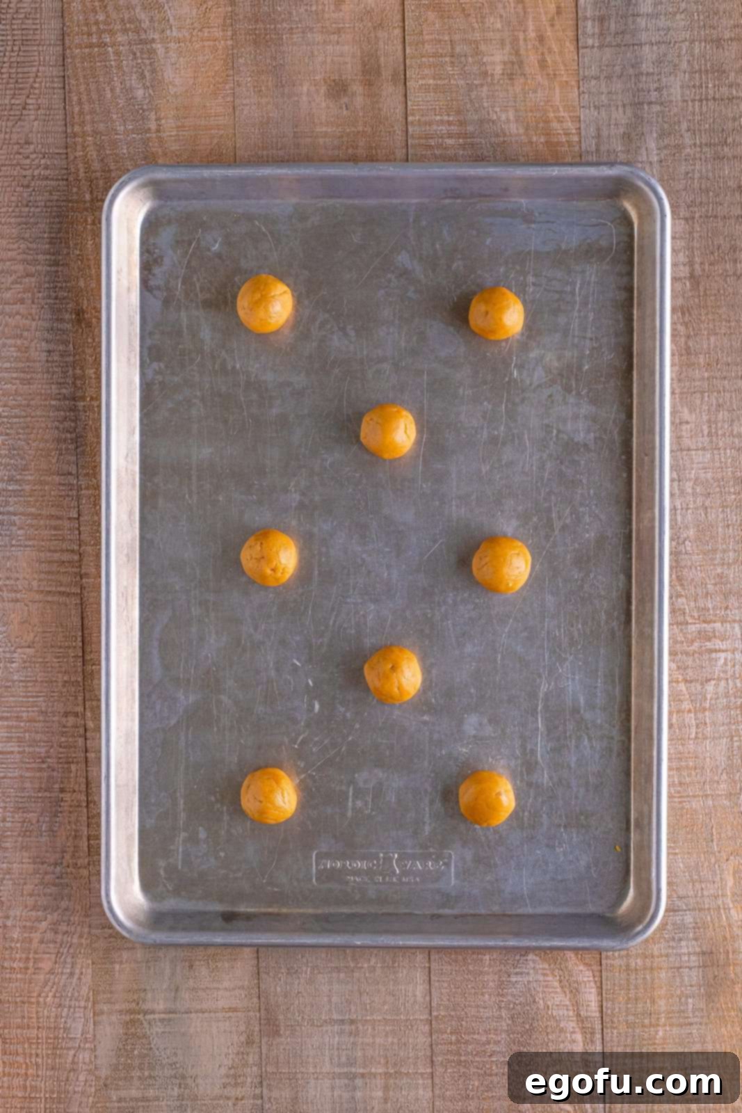 Red Nosed Reindeer Treats 9 rolls of peanut butter cookie dough on a baking sheet.