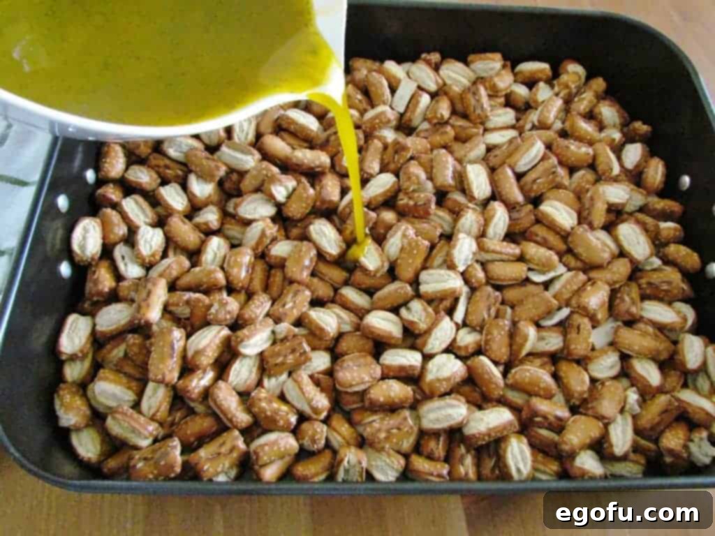 The seasoned oil mixture being poured over the pretzels in the roasting pan.