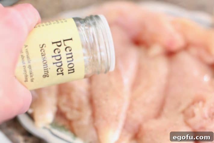 Sprinkling lemon pepper seasoning on chicken tenderloins.