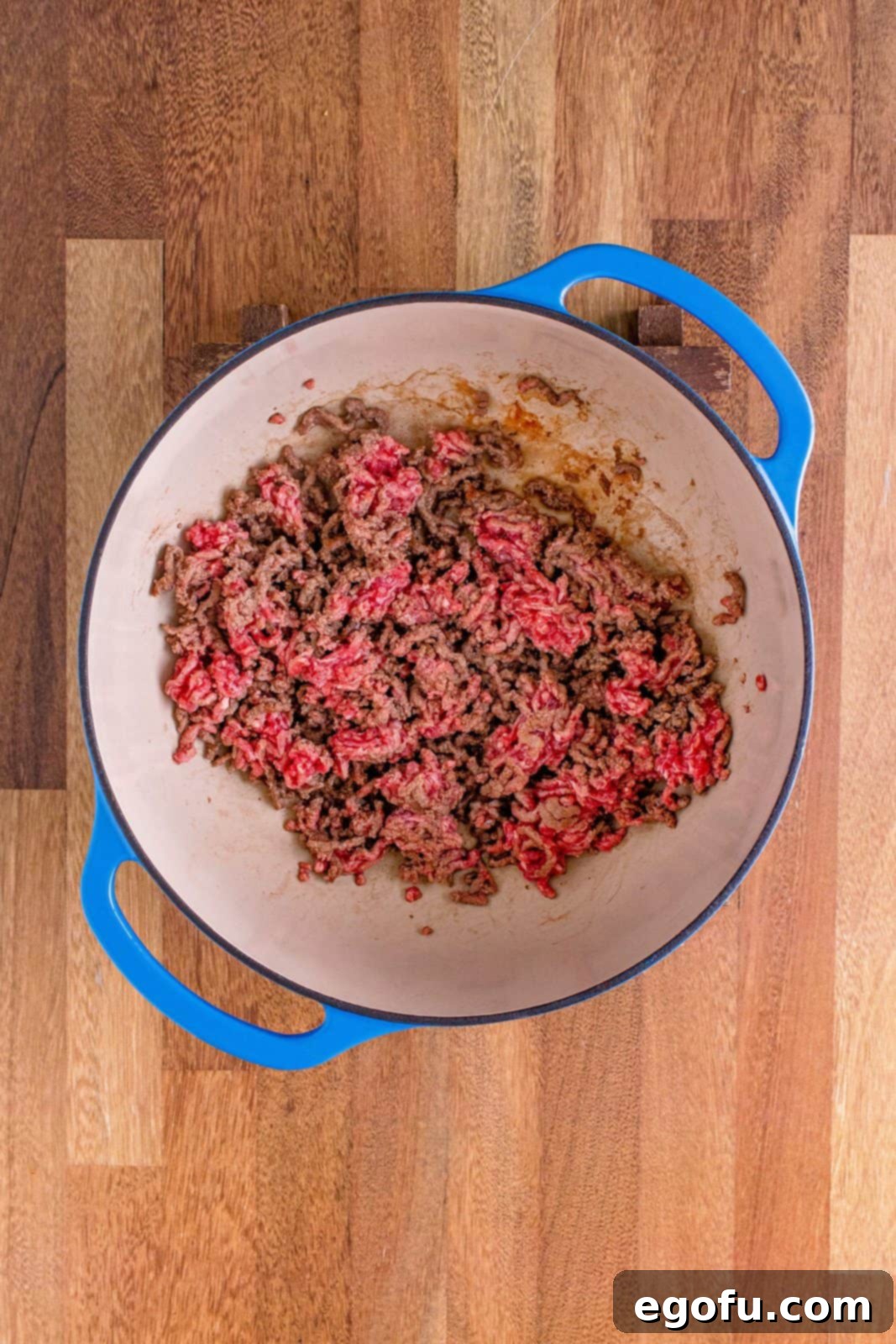 Partially browned ground beef being crumbled in a Dutch oven, cooking over medium heat.
