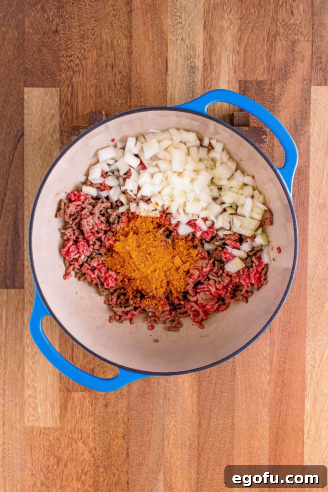 Diced onion and taco seasoning are mixed into the browning ground beef in the pot, filling the kitchen with rich aromas.