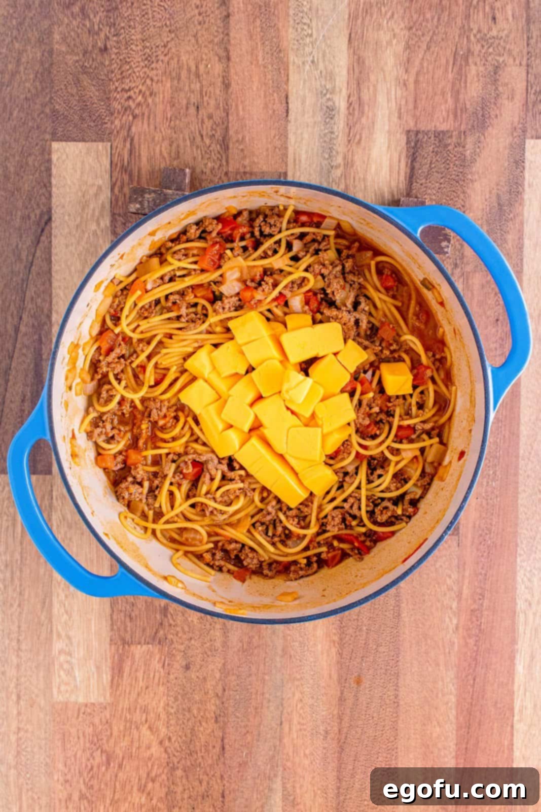 Cubed Velveeta cheese melting into the hot, cooked pasta in the Dutch oven, creating a smooth, creamy sauce.