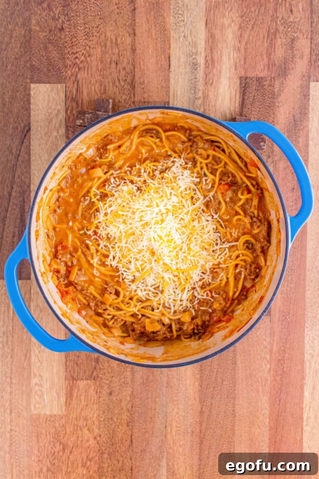 Mexican shredded cheese being stirred into the finished pasta mixture in the Dutch oven, melting into a gooey texture.