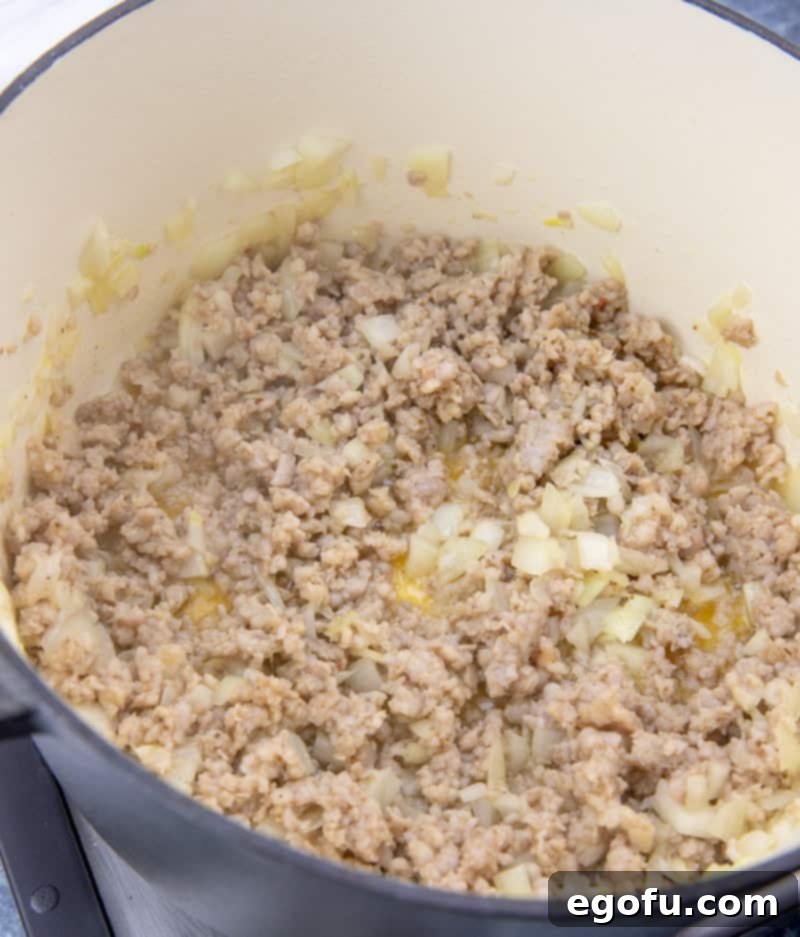 Ground sausage browning and crumbling in a Dutch oven with diced onions, creating an aromatic base for the chowder.