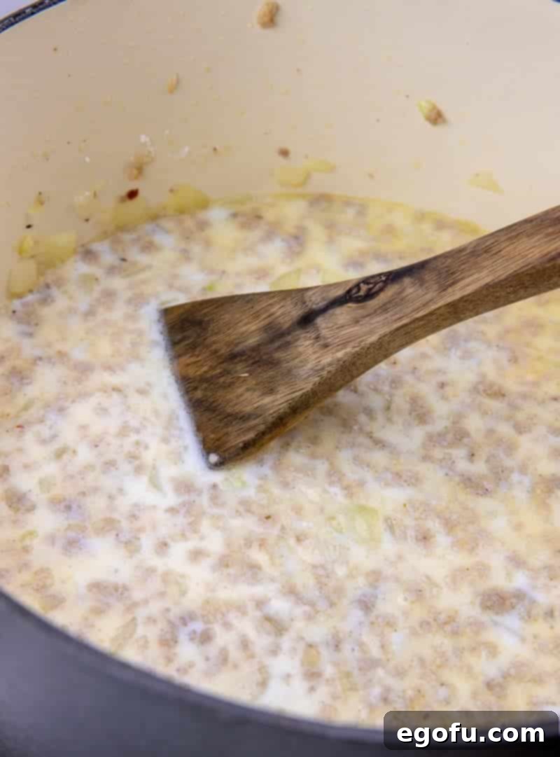 Milk and flour mixture being stirred into cooked sausage and onions in a Dutch oven, creating a creamy base for the chowder.