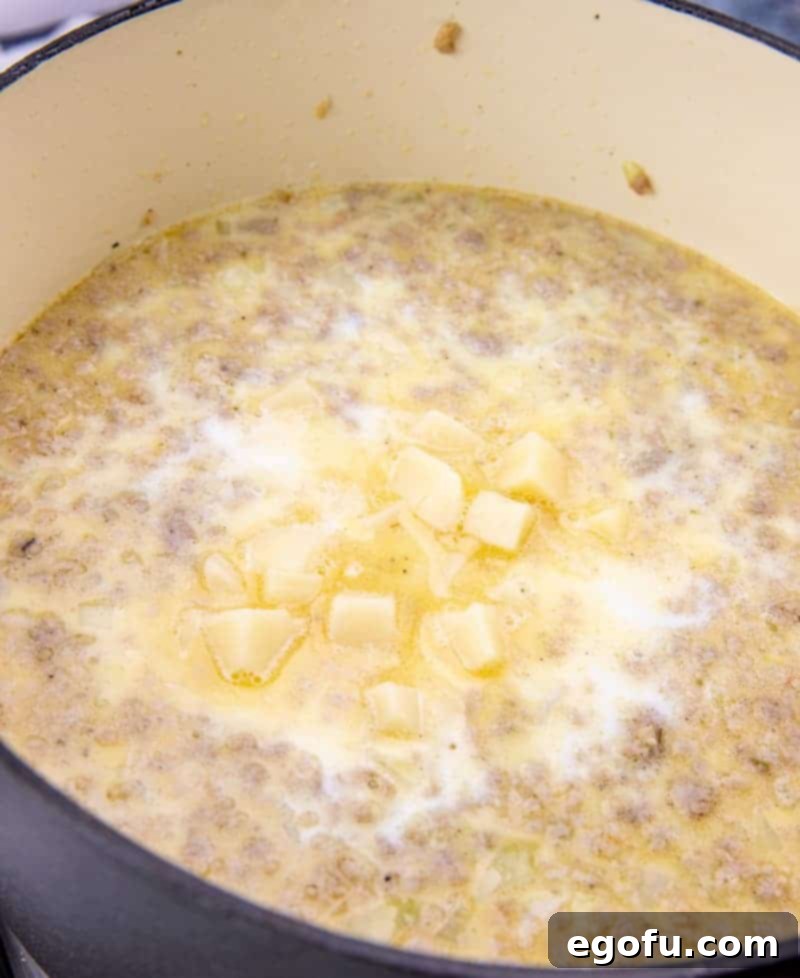 Diced potatoes and creamed corn added to the creamy sausage mixture in a Dutch oven, ready to simmer.