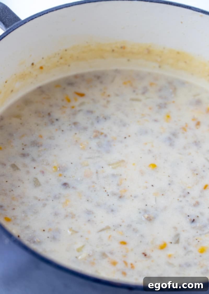 Sausage corn chowder gently simmering in a blue Dutch oven, showing its rich, thick texture.