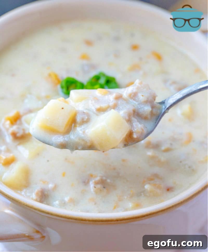 A spoonful of creamy sausage corn chowder hovering over a bowl of the finished soup, ready to be enjoyed.