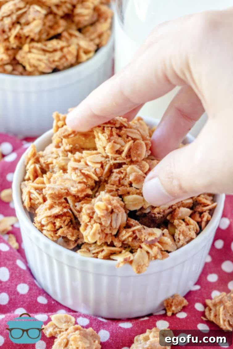 A hand reaching into a white bowl to grab some freshly made, chunky homemade granola clusters.