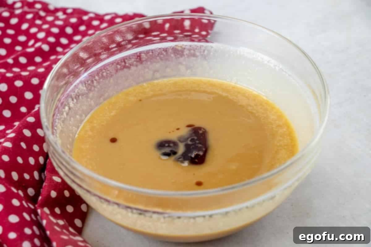 Vanilla extract being added to the melted butter, honey, and peanut butter mixture, which is now smooth and golden.