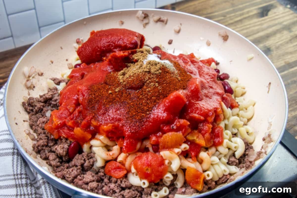 cooked macaroni noodles, tomato sauce, garlic, chili powder, and diced tomatoes added to cooked ground beef in the saucepan, blending into a chili base.