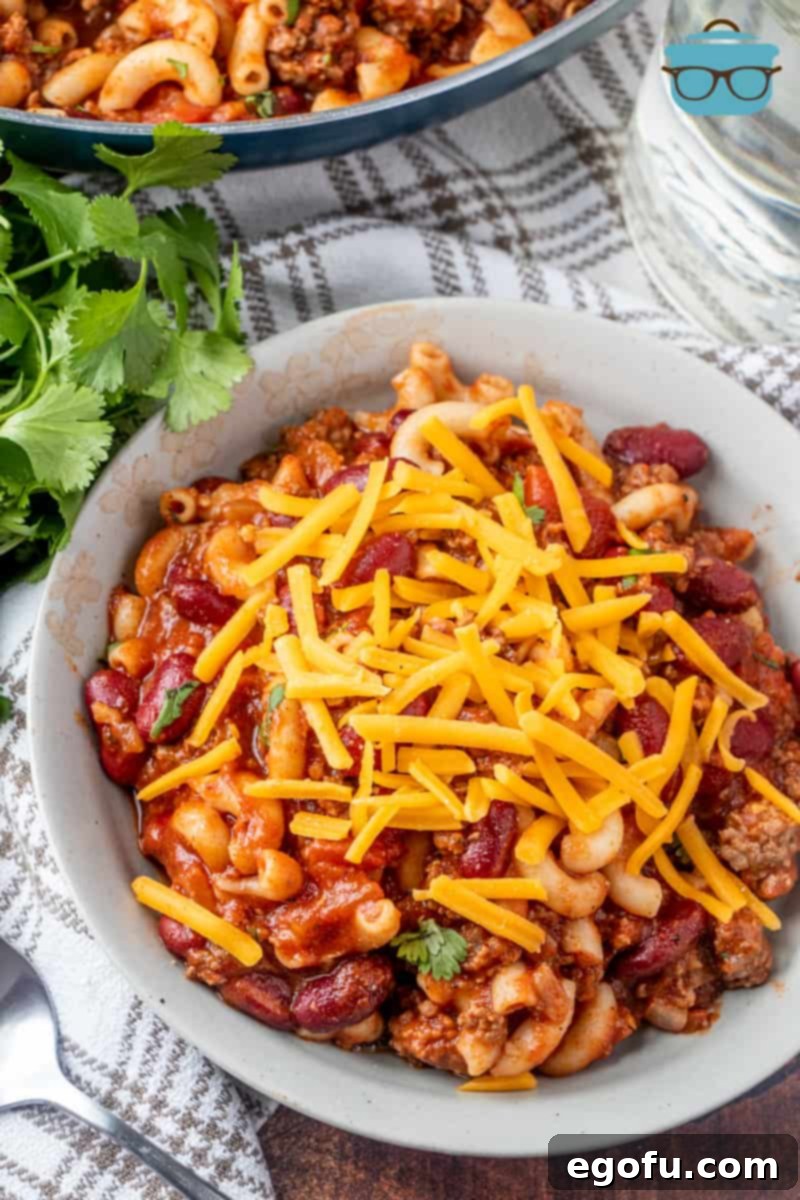 a bowl of chili Mac with shredded cheese on top, ready to eat.