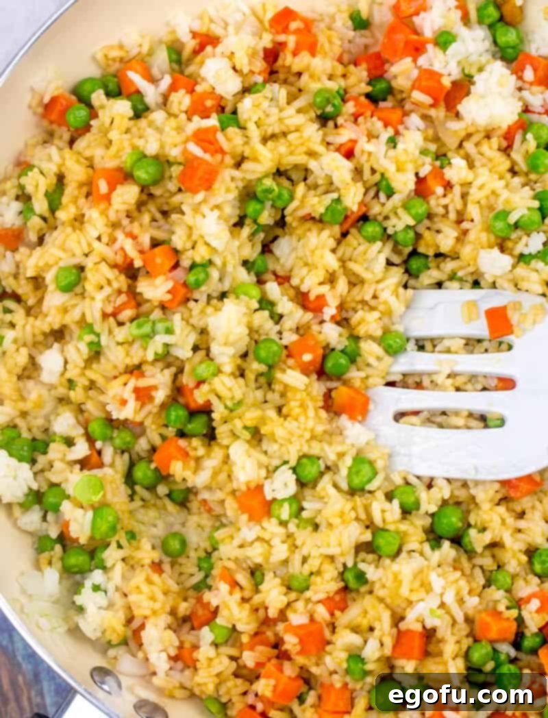 Vibrant Veggie Fried Rice 11 Soy sauce being added to the mixture of rice, peas, carrots, and onions in a skillet, ready to be stirred and seasoned for the fried rice.