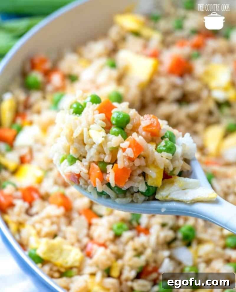 Vibrant Veggie Fried Rice 12 A spoonful of Easy Homemade Vegetable Fried Rice being lifted from a large skillet, showcasing the perfectly cooked grains, vegetables, and egg pieces.
