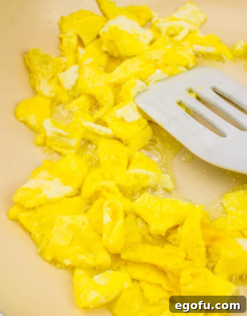 Vibrant Veggie Fried Rice 7 Cooked egg pieces being removed from a large skillet with a white spatula, ready to be set aside for the fried rice.