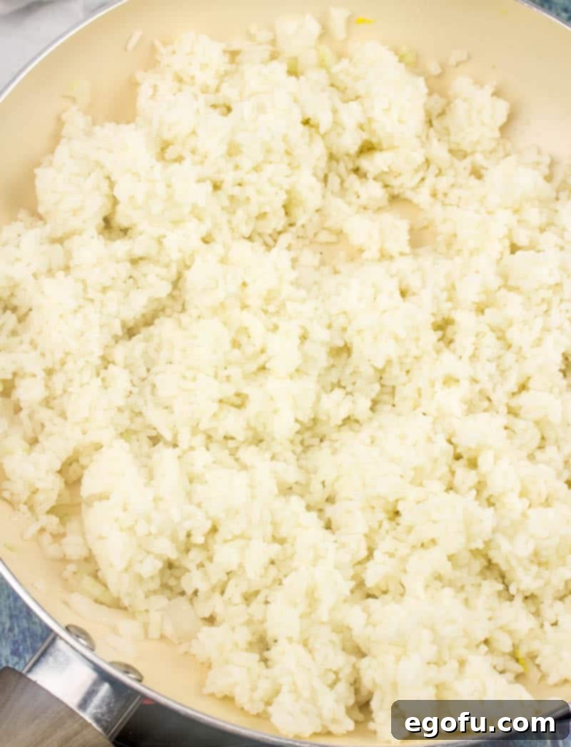 Vibrant Veggie Fried Rice 9 Cooked white rice mixed with diced onions in a large skillet, being stirred to combine and heat through, forming the base of the fried rice.