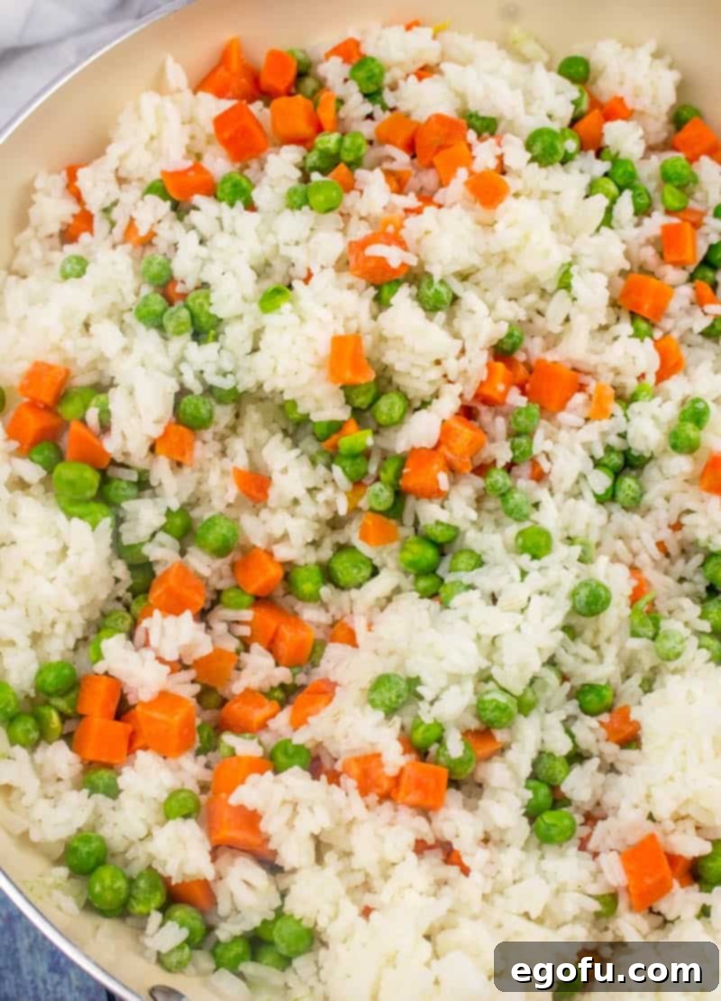 Vibrant Veggie Fried Rice 10 Frozen peas and carrots added to the cooked rice and onions in a large skillet, being stirred to incorporate into the developing fried rice.