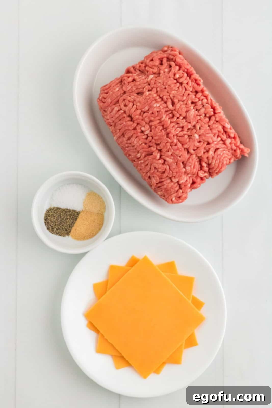 An assortment of ingredients laid out, including ground beef, salt, pepper, garlic powder, onion powder, and slices of cheddar cheese, ready for making Air Fryer Hamburgers.