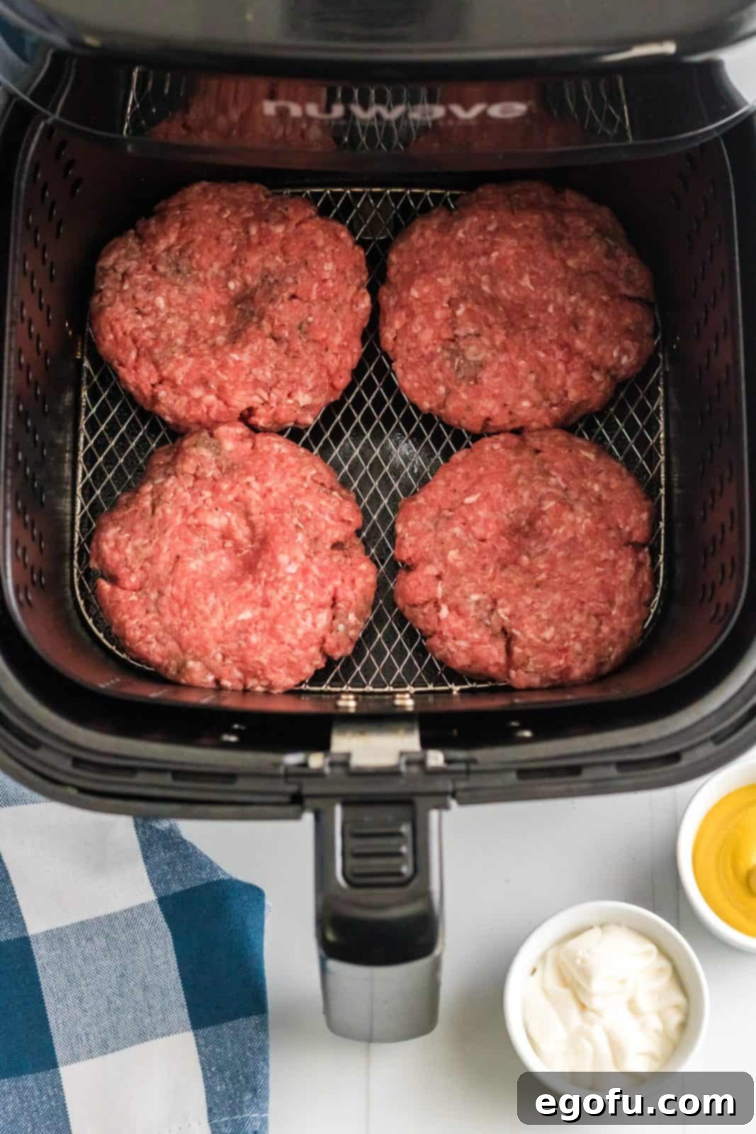 Raw hamburger patties, each with a small dent in the center, carefully arranged in the air fryer basket, ready for cooking.