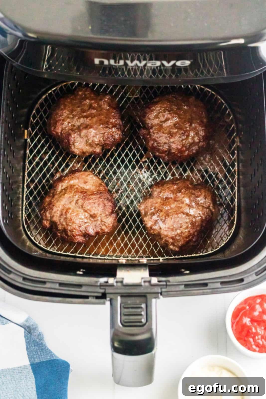 Several cooked hamburgers resting in the air fryer basket, showing a nicely browned exterior, indicating they are almost ready.