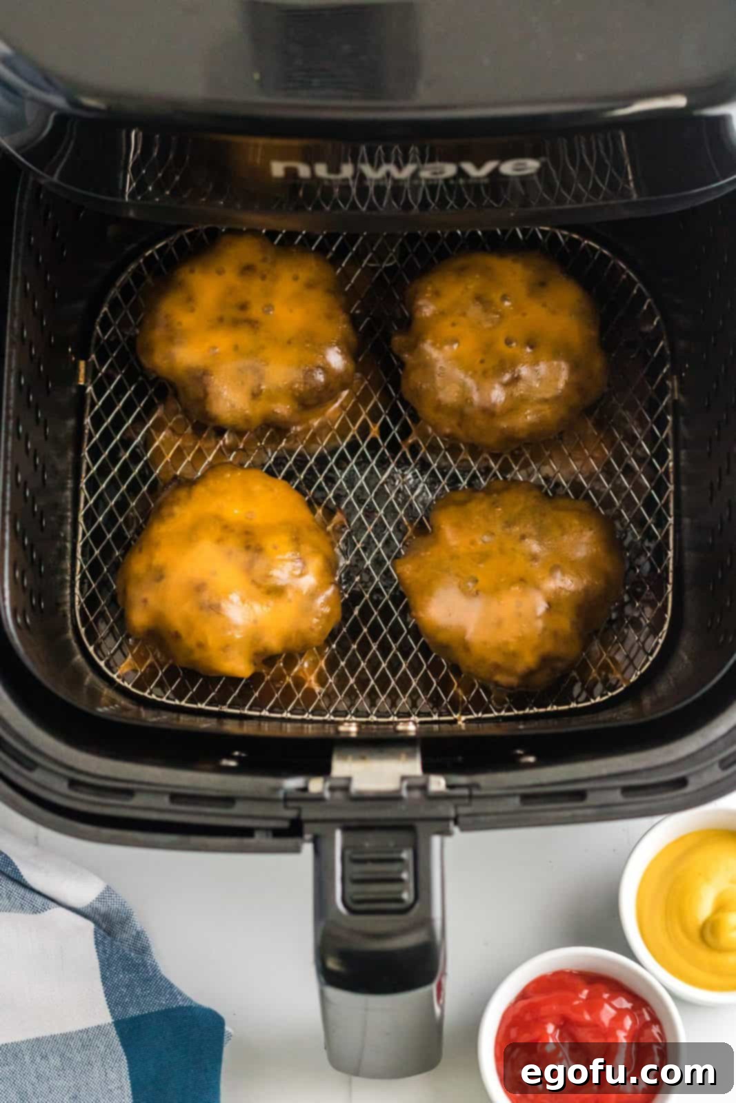 Golden-brown Air Fryer Hamburgers with perfectly melted cheddar cheese on top, still in the air fryer basket, ready to be removed and served.