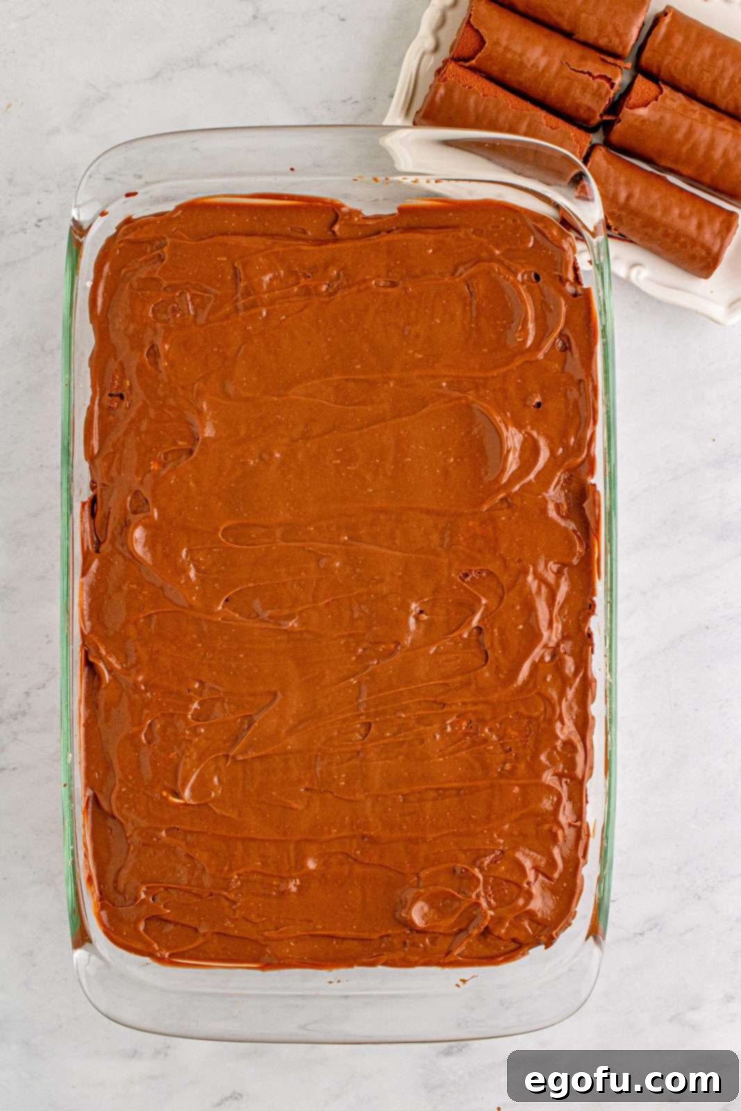 Easy No-Bake Swiss Roll 11 Chocolate pudding spread on top of cut swiss cake rolls.