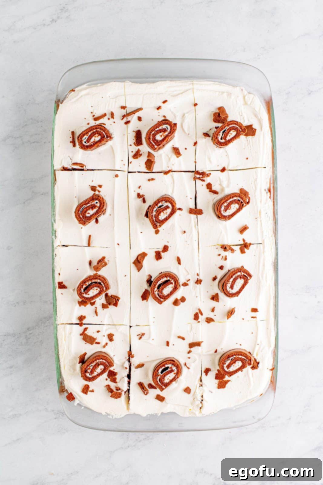 Easy No-Bake Swiss Roll 14 Finished No-Bake Swiss Roll Cake topped with cut swiss cake rolls and chocolate, cut into slices.