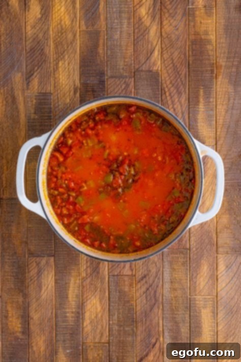 Simmering rich tomato mixture in a pot, covered, allowing flavors to meld.