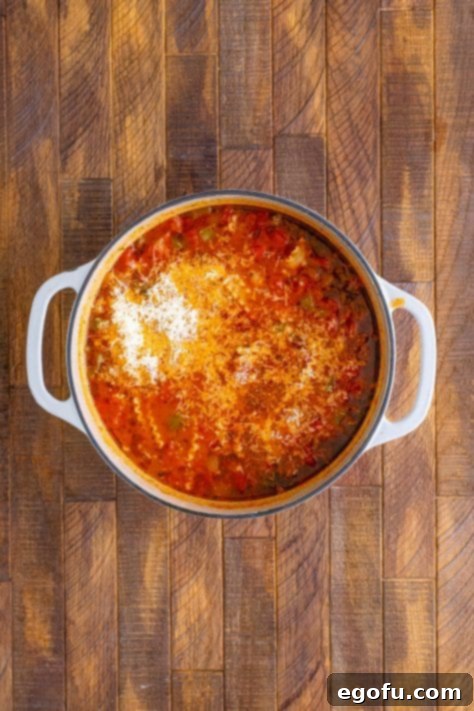 Freshly grated Parmesan cheese being stirred into the hot lasagna soup in the pot.
