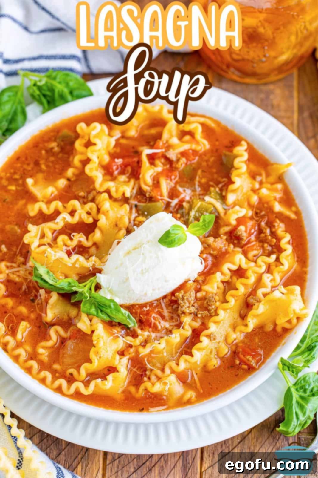 An inviting overhead view of a white bowl overflowing with rich Lasagna Soup, generously topped with a dollop of creamy ricotta cheese and fresh basil leaves.