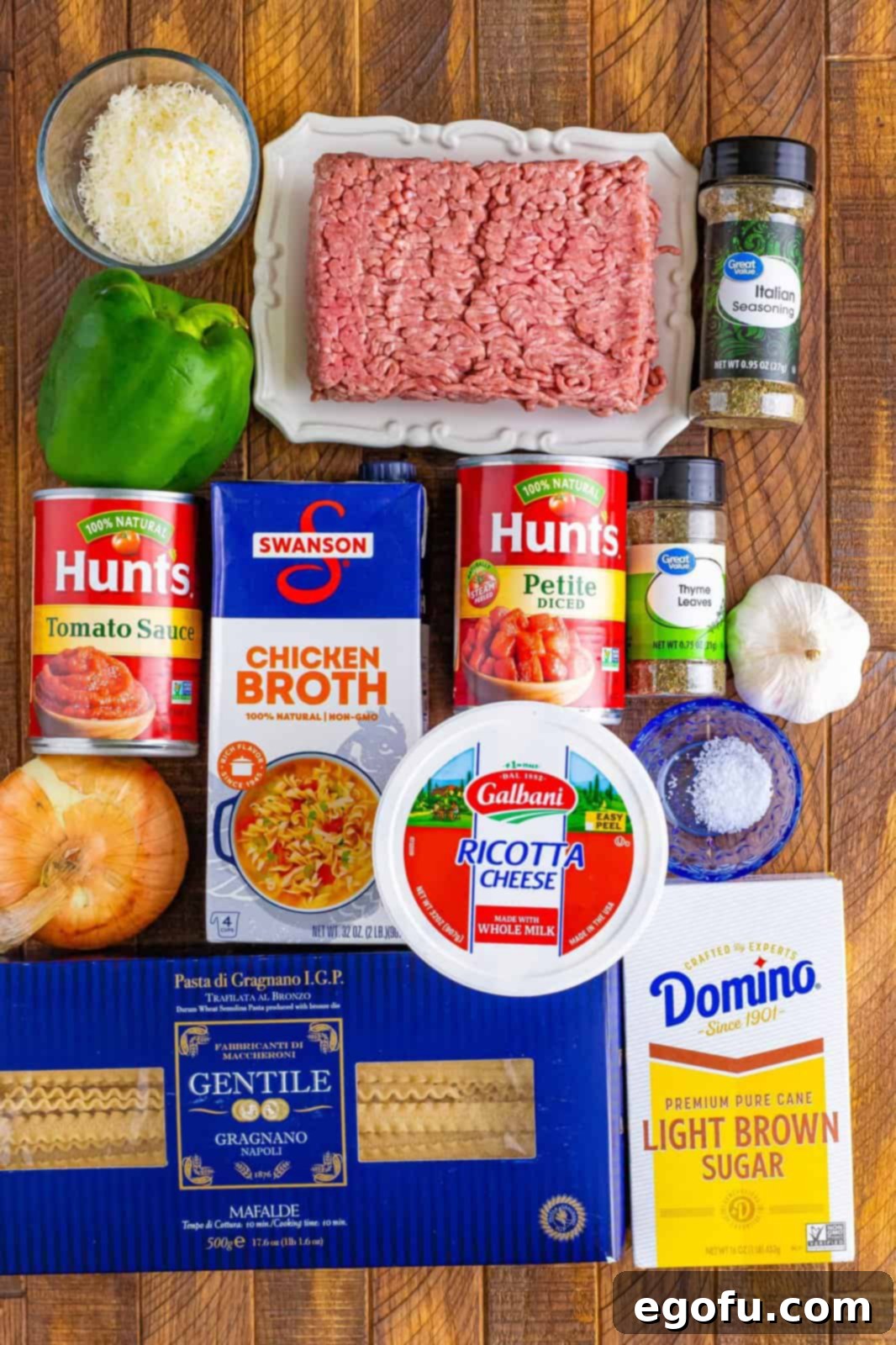 A vibrant flat lay of all the fresh and pantry ingredients needed for Lasagna Soup: ground beef, onion, green pepper, chicken broth, tomato sauce, garlic, thyme, diced tomatoes, parmesan cheese, mozzarella cheese, and Italian seasoning.
