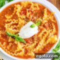 A white bowl filled with comforting lasagna soup, artfully topped with creamy ricotta cheese and a sprinkle of fresh herbs.