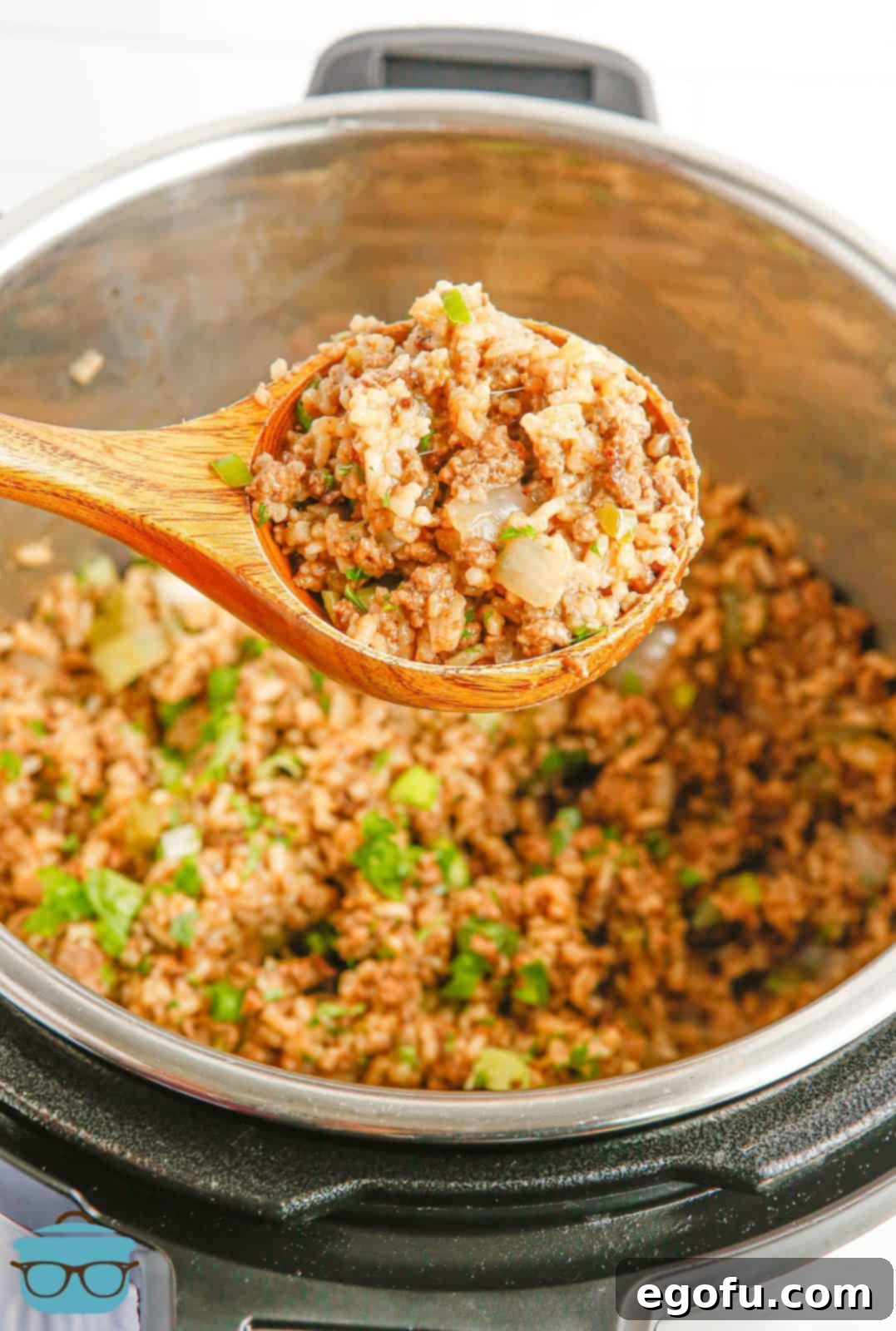 Wooden spoon holding up a scoop of Instant Pot Dirty Rice, showcasing its rich, savory texture and color, garnished with green onions.