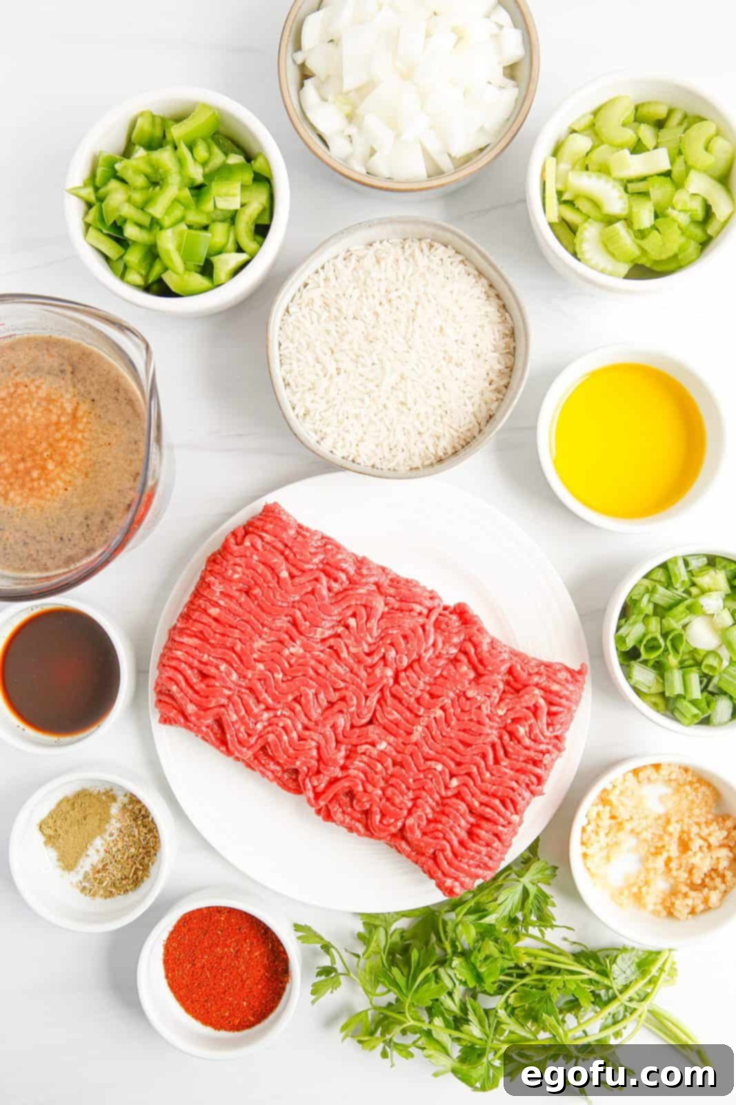 A vibrant flat lay of all the essential ingredients needed for Instant Pot Dirty Rice: raw ground beef, a bottle of olive oil, a yellow onion, green bell pepper, celery stalks, fresh garlic cloves, small bowls of thyme and oregano, a shaker of Creole seasoning, Worcestershire sauce, salt, pepper, uncooked long grain white rice, a carton of beef broth, a single bay leaf, and fresh green onions and parsley for garnish.