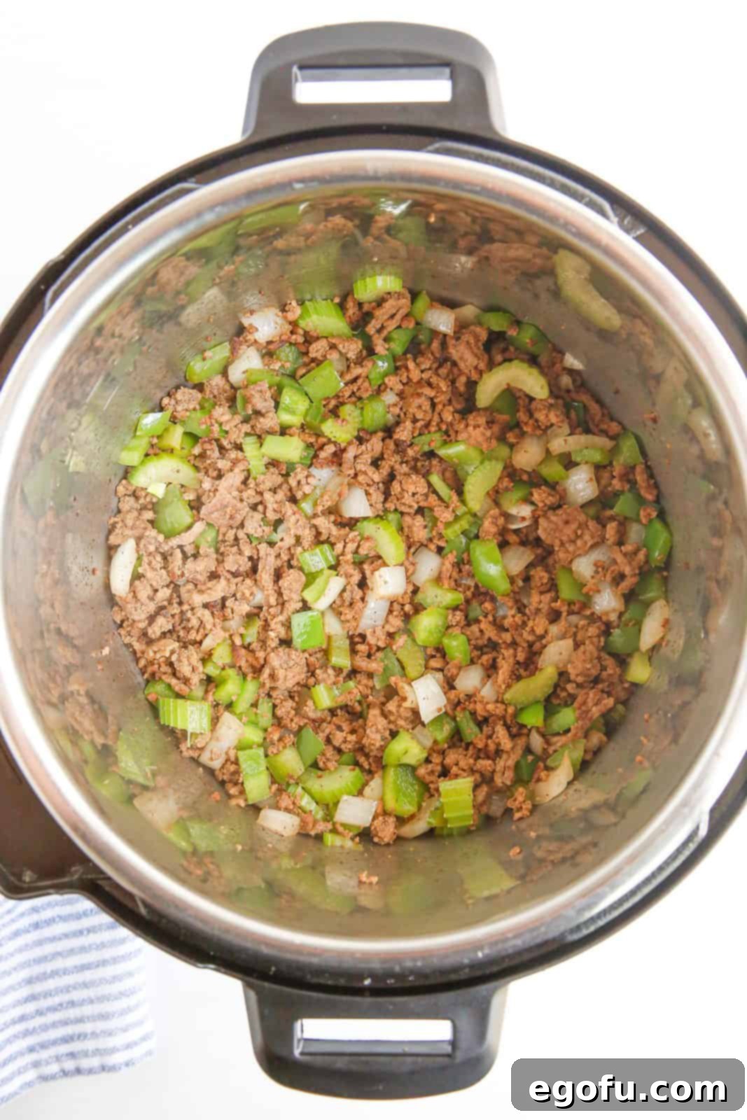 A close-up view of the ground beef, diced onions, celery, and bell pepper mixture sautéed to perfection in the Instant Pot, fragrant and ready for the next layer of ingredients.