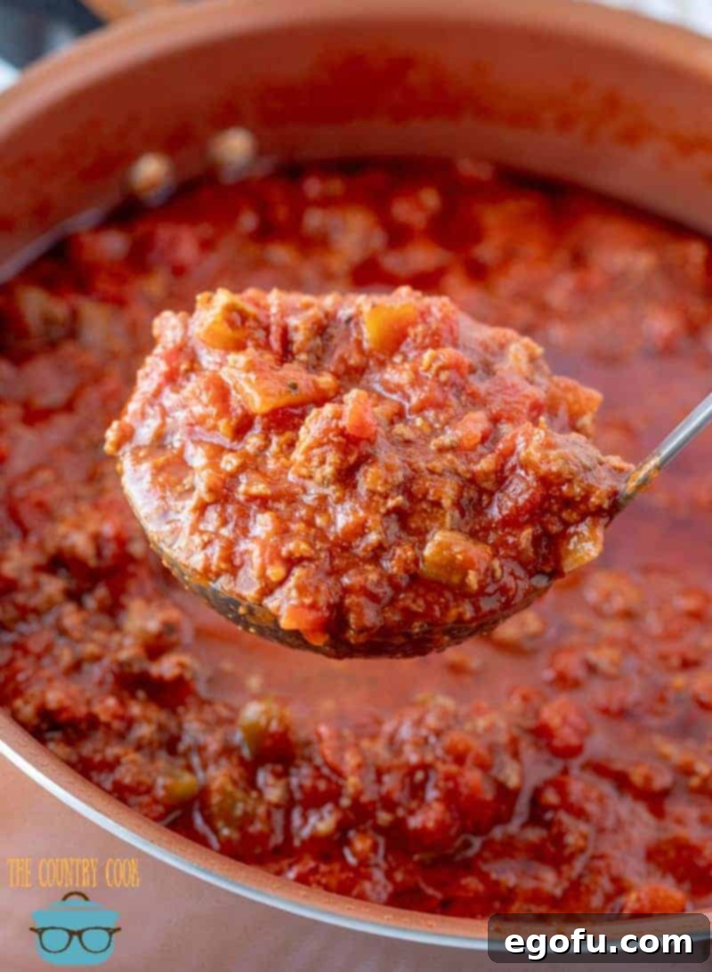a sauce spoon holding up beefy spaghetti sauce over a pot.