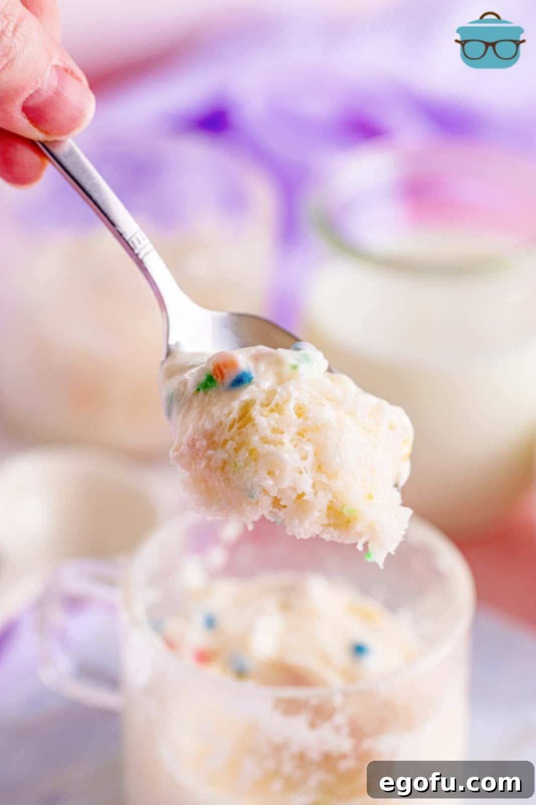 A spoon holding up a piece of fluffy mug cake over a clear mug.