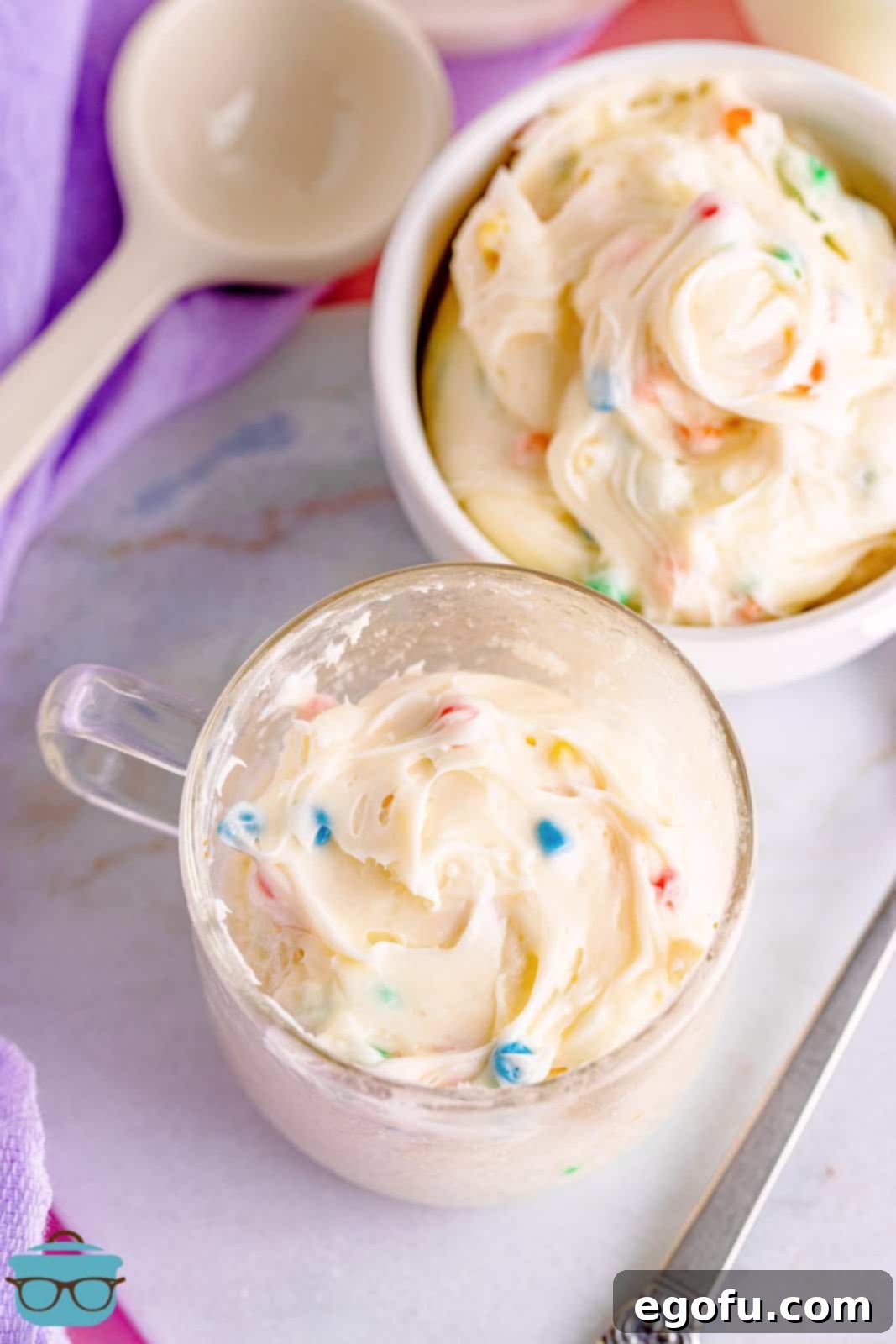 Baked microwave mug cake topped with frosting, set on a marble surface.