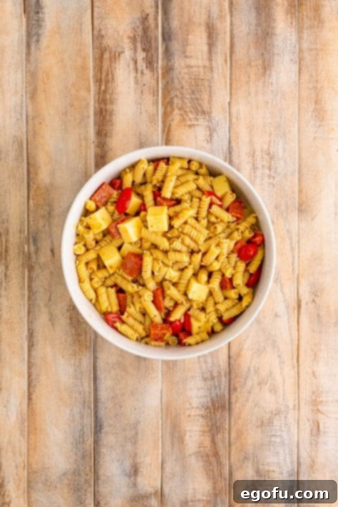 Italian dressing, pasta, cheese, tomatoes, and pepperoni in a bowl.