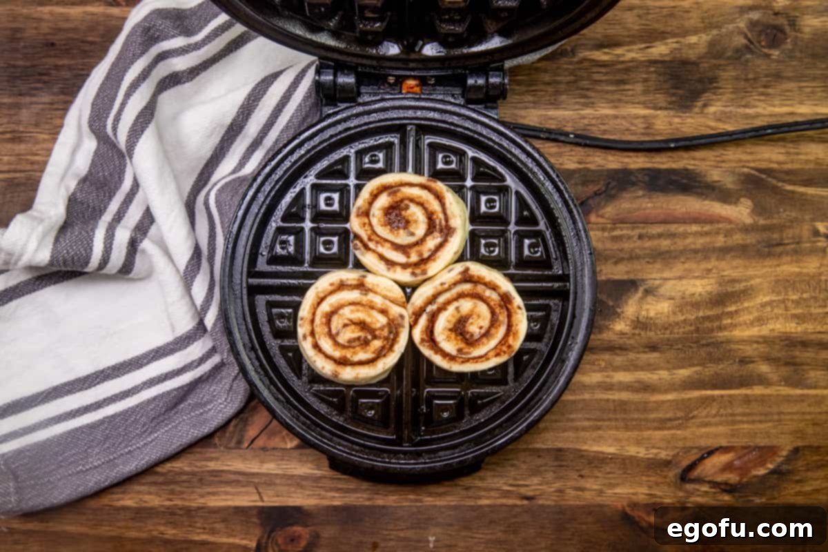 three refrigerated cinnamon rolls on a waffle maker.