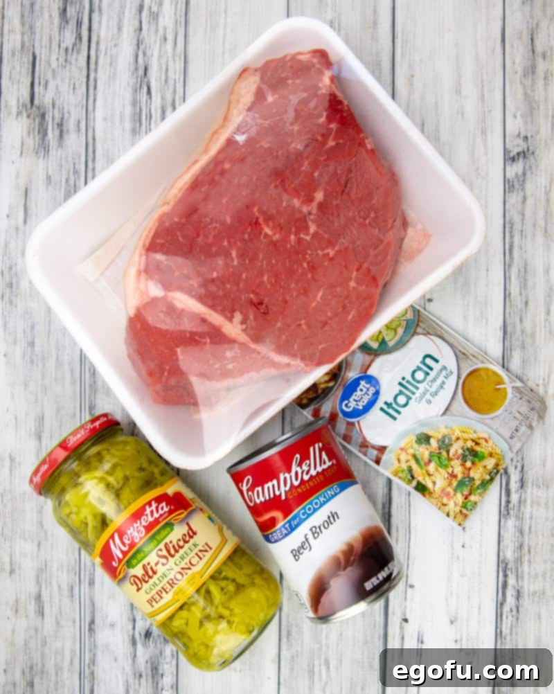 Chuck roast, beef broth, Italian seasoning packet, provolone cheese, and sub rolls laid out on a table, ready for cooking.